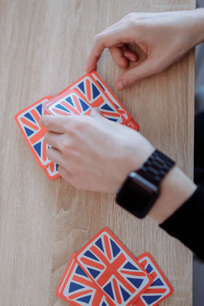 Person with smartwatch playing card game featuring British flag design on wooden table.